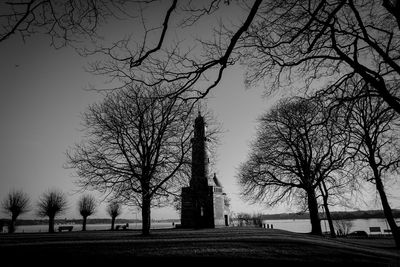 Low angle view of silhouette bare trees and lighthouse against sky