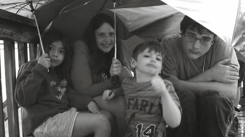 Siblings sitting under umbrella during monsoon