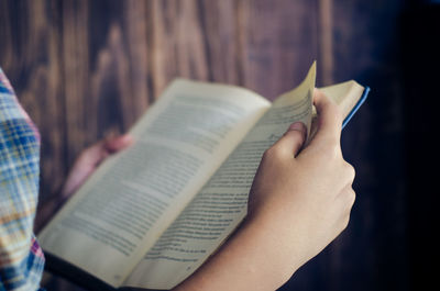Cropped hands of woman reading book against wall