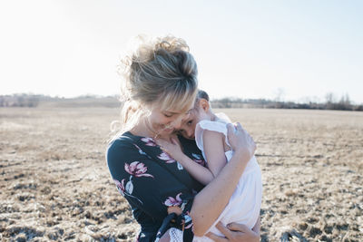 Mother holding her daughter close whilst standing in a field at sunset