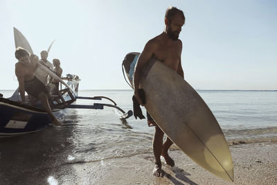 Adult men carrying surfboards while unloading vessel