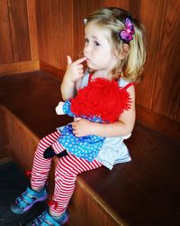 Girl holding doll while sitting on wooden seat