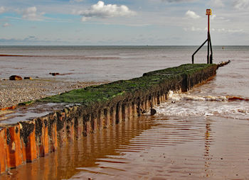 Wooden posts on beach against sky