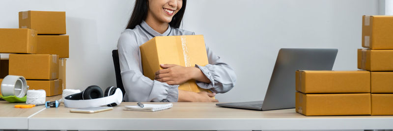 Young woman holding box while sitting at office