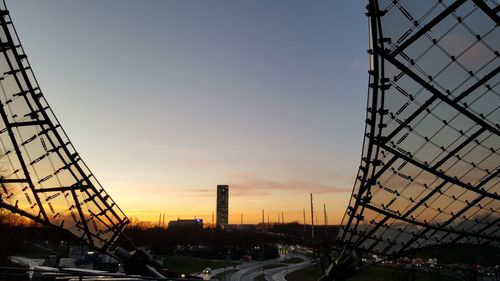 Silhouette bridge by buildings against sky during sunset