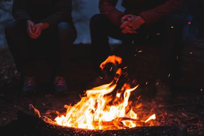 Low section of friends sitting at campfire during night
