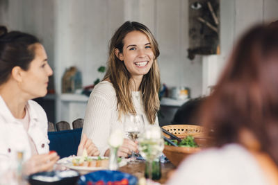 Happy young female friends enjoying at dining table during lunch party