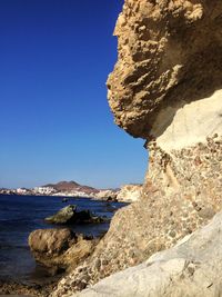 Rocky cliff by sea against clear blue sky