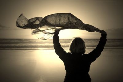 Rear view of silhouette woman waving scarf against sea