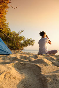 Rear view of woman sitting on beach against clear sky