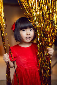 Portrait of a beautiful korean baby girl in a red dress at christmas with a gold decoration