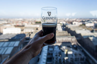 Close-up of hand holding drink against cityscape