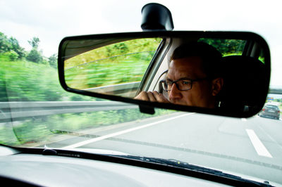 Reflection of young man on rear-view mirror in car