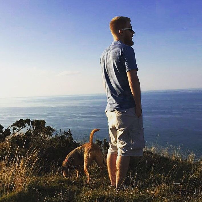 SIDE VIEW OF MAN WITH DOG STANDING ON SHORE