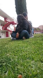 Rear view of friends sitting on field against clear sky