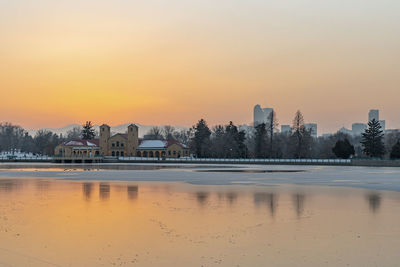 Scenic view of lake by buildings against sky during sunset