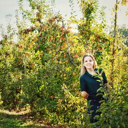 Portrait of smiling young woman standing by apple trees