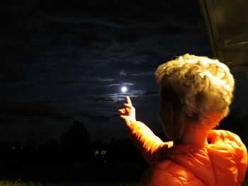 Close-up of hand holding illuminated lighting equipment against sky at night