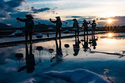 Silhouette people standing on salt flat against sky during sunset