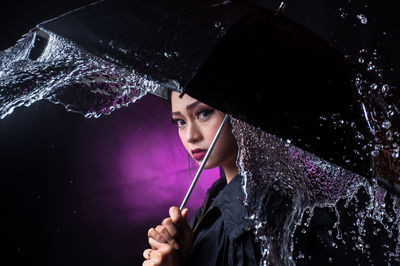 Portrait of young woman holding wet umbrella against purple background