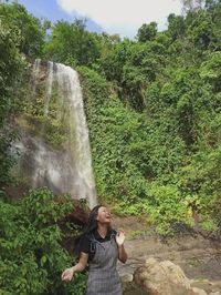 Young woman standing against waterfall in forest