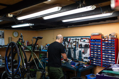 Back view of bald man standing near workshop while fixing bicycle in modern professional garage