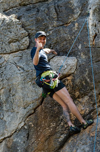 Low angle portrait of man gesturing while rock climbing