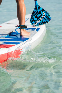 Crop anonymous female surfer standing on surfboard and rowing with paddle while practicing on surface of sea in summer