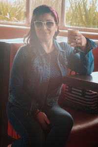Young woman wearing sunglasses sitting on seat at home
