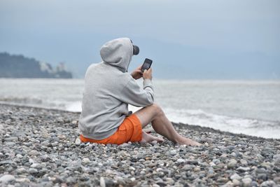 Full length of man photographing sea through mobile phone at beach