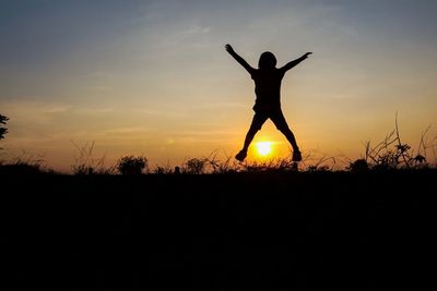 Silhouette playful boy jumping on grassy field against sky