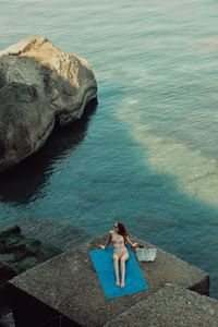 High angle view of woman sitting on rock by sea