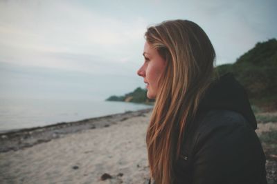 Side view of young woman standing at beach against sky
