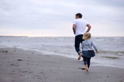 Father and daughter playing at beach against sky