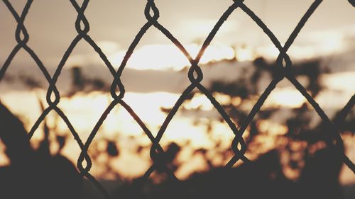 Close-up of chainlink fence against sky during sunset