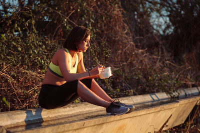 Side view of young woman sitting on tree