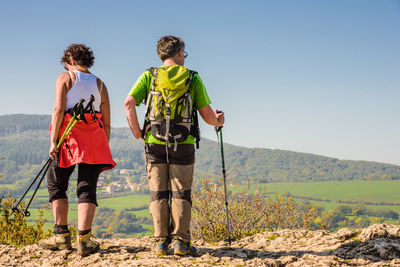 Rear view of couple with hiking poles standing on cliff against clear sky