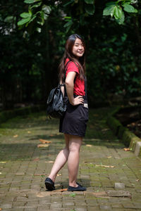 Full length of smiling young woman standing on footpath at park