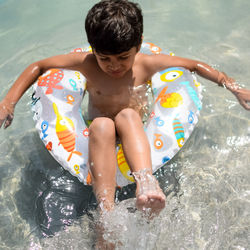 Happy indian boy swimming in a pool, kid wearing swimming costume along with air tube during day
