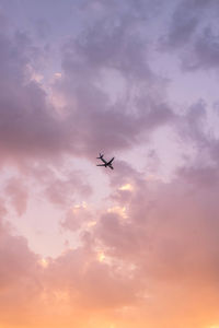 Low angle view of silhouette airplane flying against cloudy sky during sunset