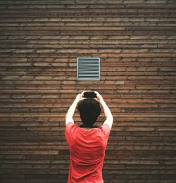 Rear view of man photographing window on wooden wall