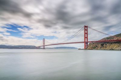 Bridge over river against cloudy sky