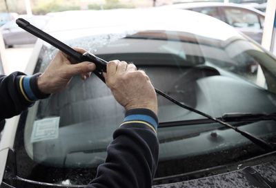 Cropped hands of mechanic holding windshield wiper against car at auto repair shop