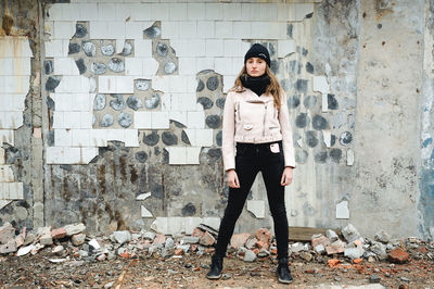 Full length portrait of young woman standing against wall