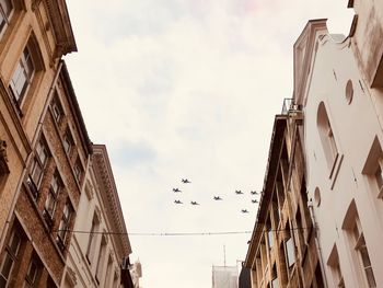 Low angle view of fighter jets flying as seen from between buildings