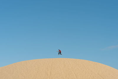 Low angle view of man jumping over desert against clear sky