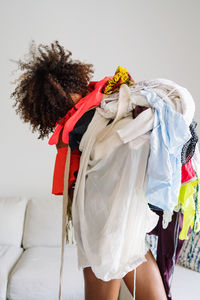 Black woman with afro hair holding pile of clothing standing in the living room