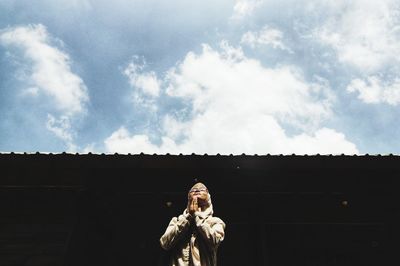 Low angle view of young woman standing against building against sky