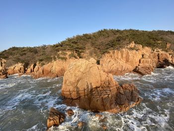 Rock formation by sea against clear sky