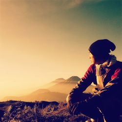 Man sitting on mountain against sky during sunset